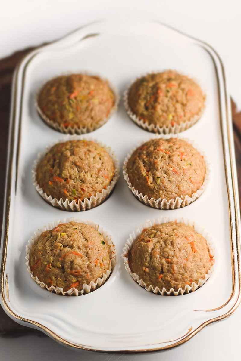 Six freshly baked zucchini carrot oatmeal muffins in white paper liners, arranged neatly on a white tray.