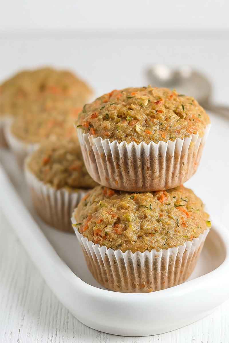 A stack of two zucchini carrot oatmeal muffins in white paper liners, showcasing their golden-brown tops and visible shredded carrots.