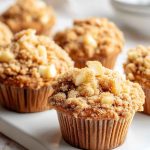 Freshly baked Apple Cinnamon Crumb Muffins arranged on a white plate, highlighting the crumbly topping and apple pieces.
