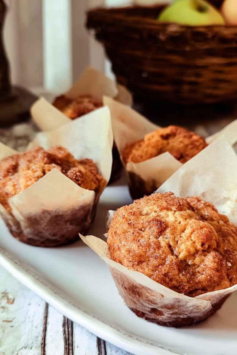 Apple cinnamon muffins in white liners on a white plate, surrounded by rustic decor.