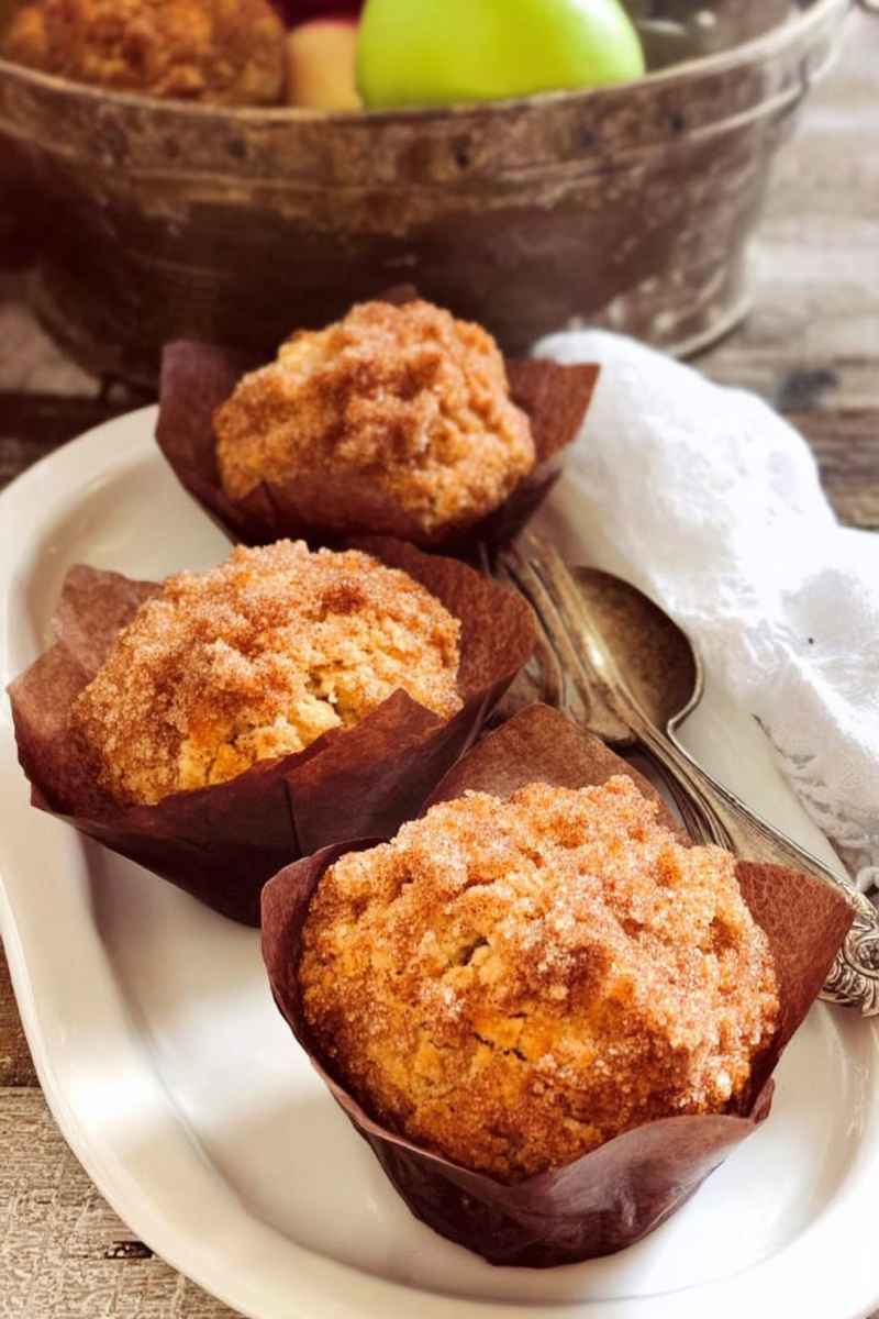 Apple cinnamon muffins on a white plate with a basket of fresh apples in the background.