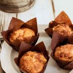 Golden-brown apple cinnamon muffins in brown paper liners on a white plate, ready to be enjoyed.