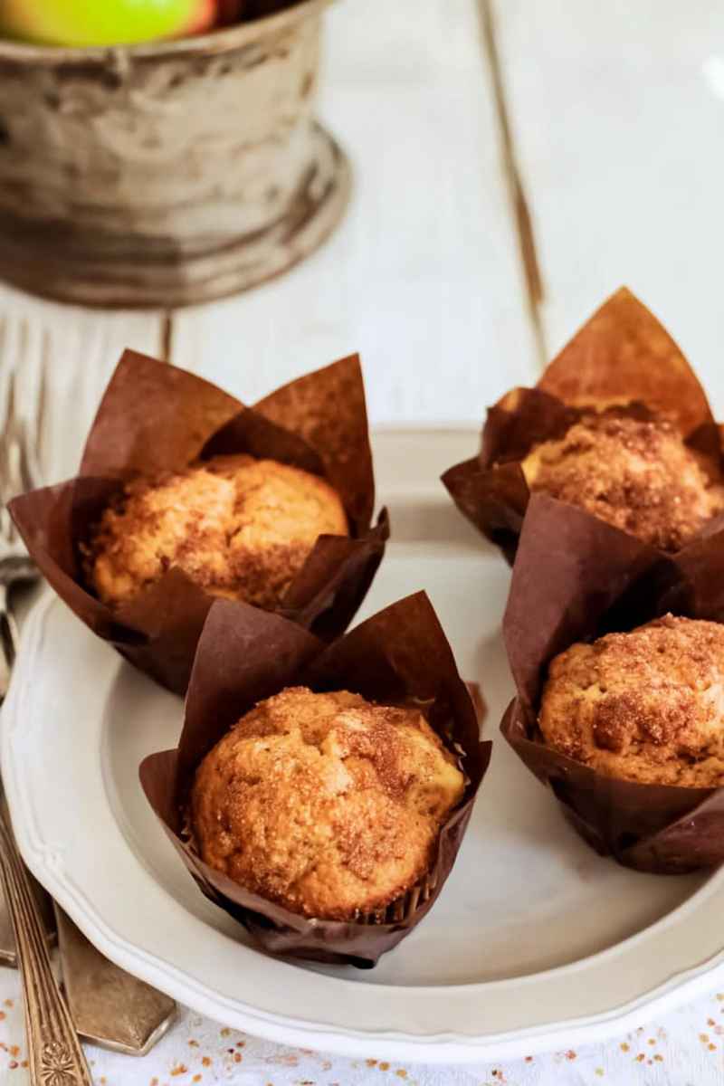 Golden-brown apple cinnamon muffins in brown paper liners on a white plate, ready to be enjoyed.