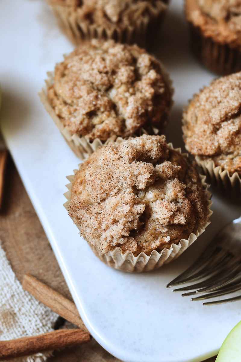 Close-up of golden Sourdough Apple Cinnamon Muffins with a crumbly cinnamon topping, placed on a white plate.
