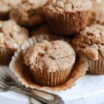 A stack of Sourdough Apple Cinnamon Muffins with a crumbly topping, surrounded by baking tools.
