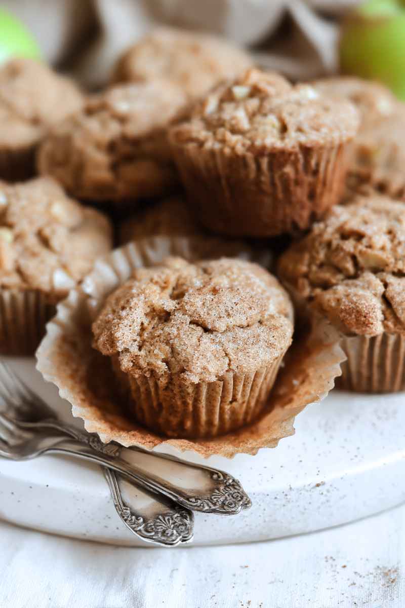 A stack of Sourdough Apple Cinnamon Muffins with a crumbly topping, surrounded by baking tools.