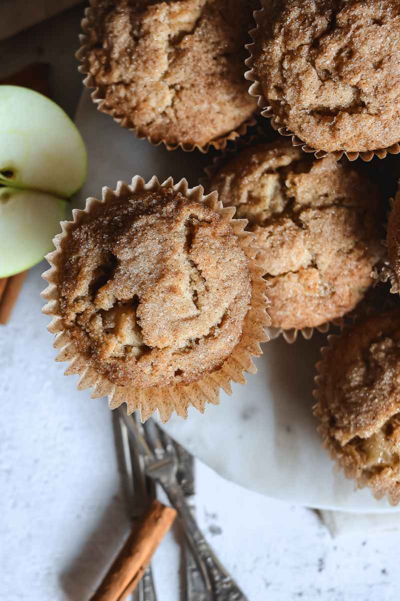 Golden Sourdough Apple Cinnamon Muffins with a crumbly topping, set against a rustic background with cinnamon sticks.