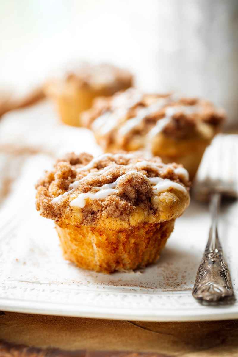 Apple Muffins with cinnamon streusel and vanilla icing drizzle on a white plate.