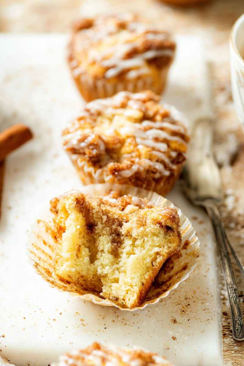 A tray of golden Apple Muffins with cinnamon streusel and vanilla icing drizzle.