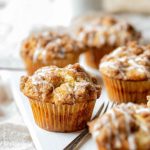 Golden-brown Apple Coffee Cake Muffins topped with cinnamon streusel and drizzled with vanilla icing.