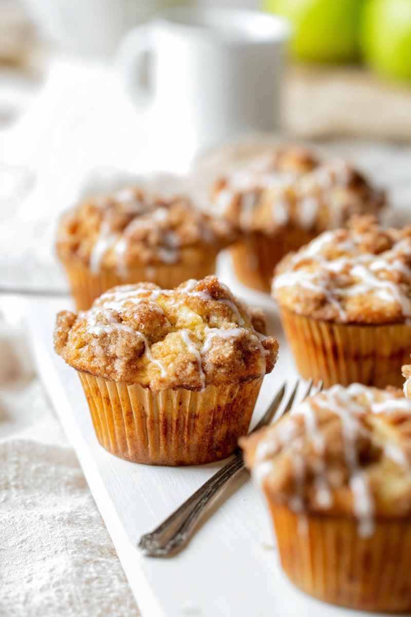 Golden-brown Apple Coffee Cake Muffins topped with cinnamon streusel and drizzled with vanilla icing.