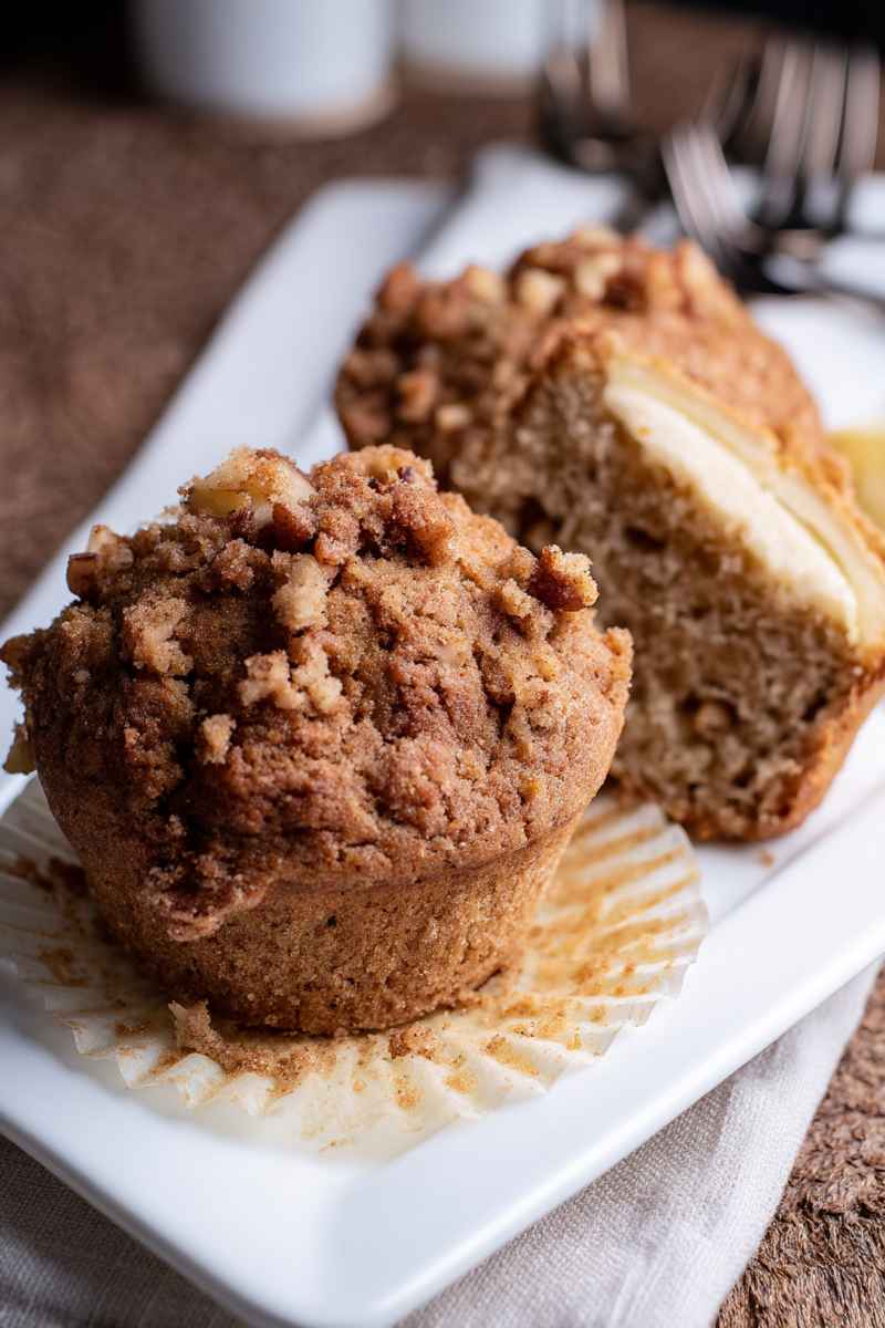 A sliced banana muffin revealing its cream cheese filling, surrounded by whole muffins with streusel topping.