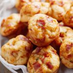 A plate of freshly baked muffins topped with bacon pieces and sprinkled with parsley.
