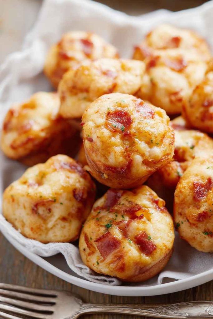 A plate of freshly baked muffins topped with bacon pieces and sprinkled with parsley.