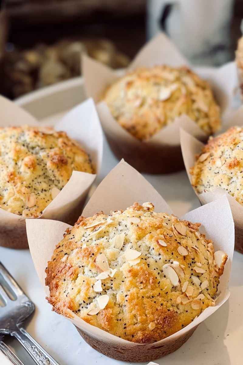 Golden Bakery-Style Almond Poppy Seed Muffins topped with sliced almonds and poppy seeds, ready to be enjoyed.