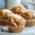 Golden banana muffins with cream cheese topping, displayed on a white plate.
