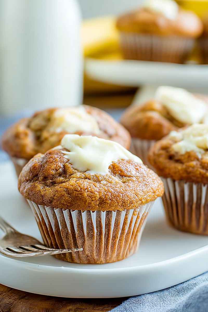 Fluffy banana muffins topped with creamy frosting, arranged neatly on a plate.
