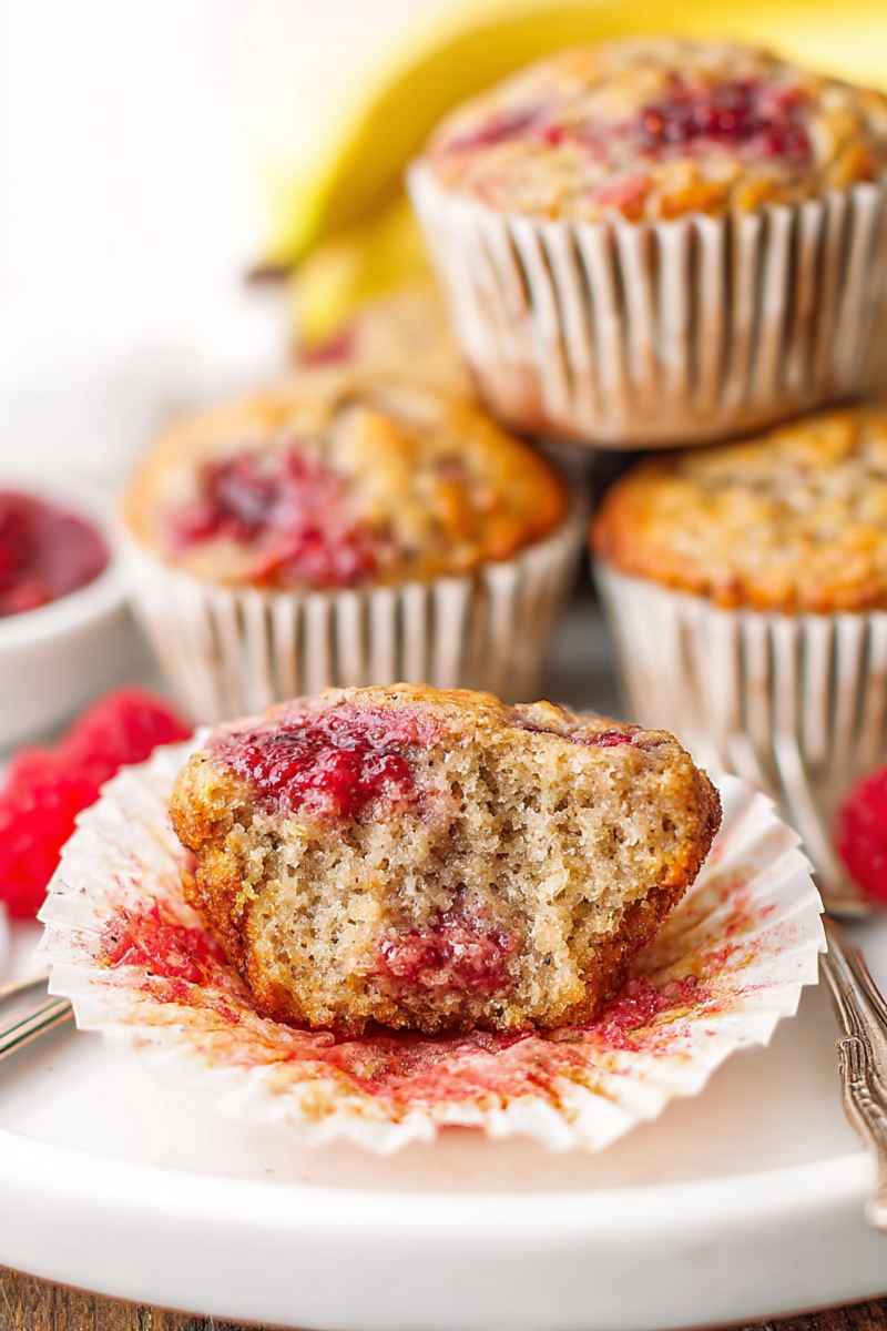 A halved banana raspberry muffin on a plate, showing the raspberry jam filling and golden exterior.