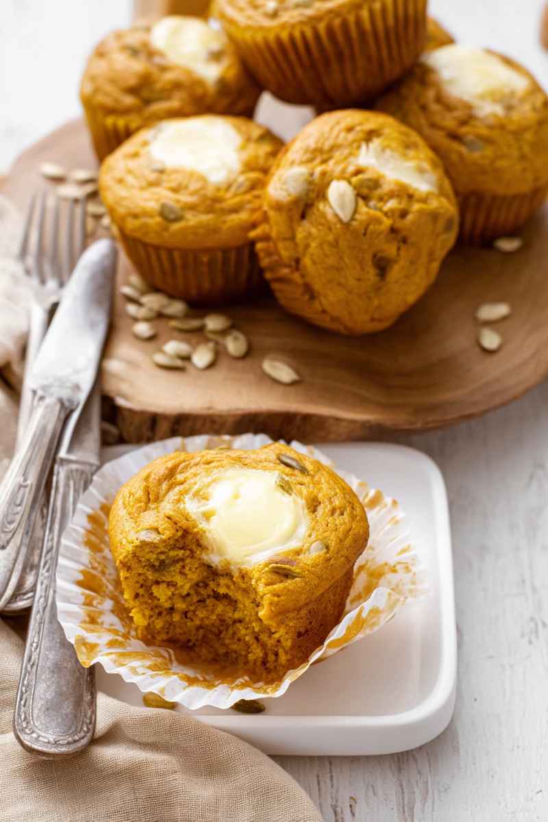 Pumpkin muffins with cream cheese filling, garnished with pumpkin seeds, served on a wooden board.