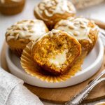 Pumpkin muffin cut in half, revealing a creamy white filling, surrounded by whole muffins.