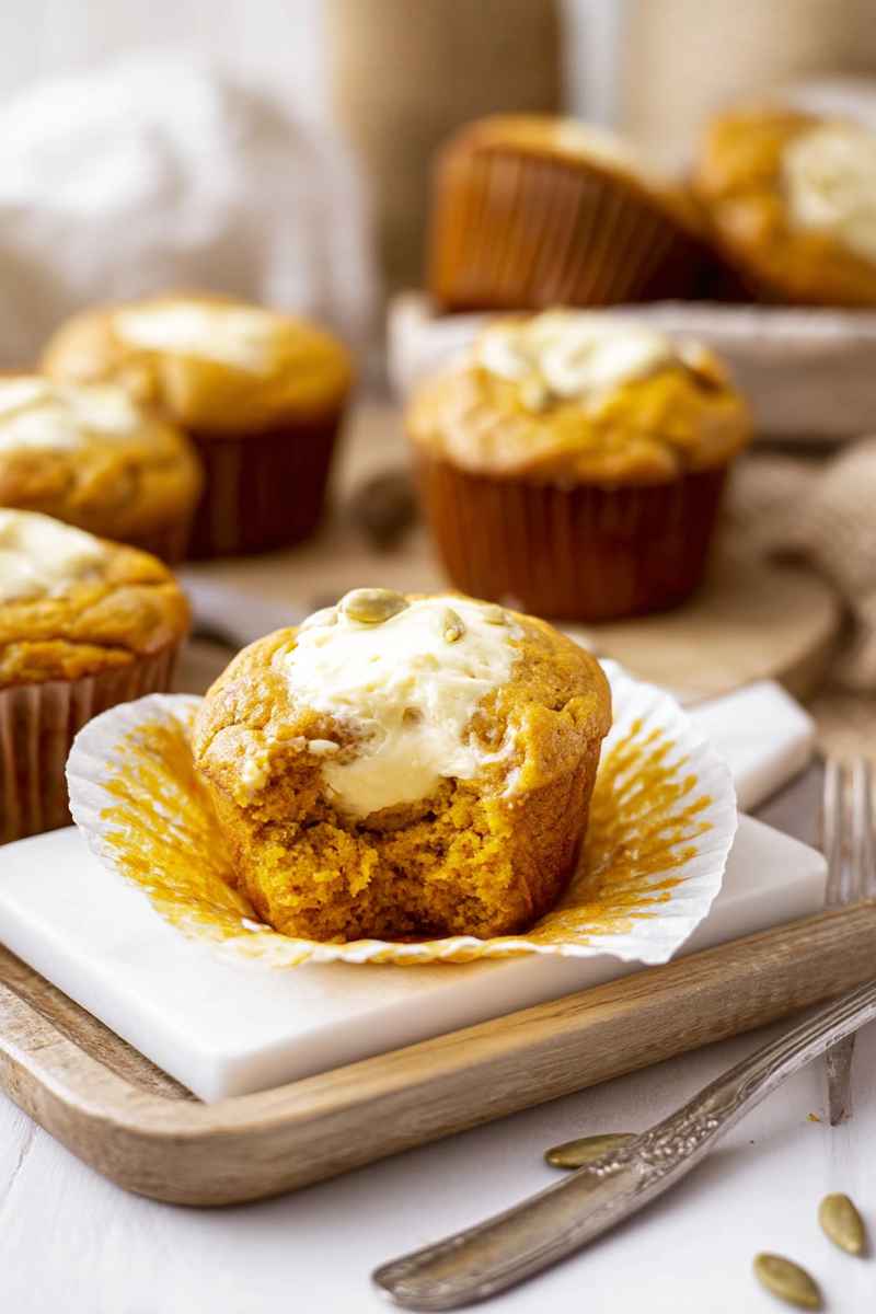 Pumpkin muffin with cream cheese frosting, placed on a white plate atop a wooden cutting board.
