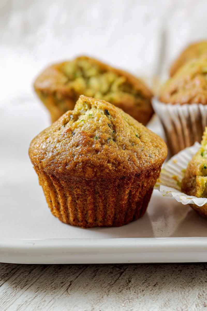 Close-up of tender zucchini muffins on a white plate, highlighting their golden-brown tops.