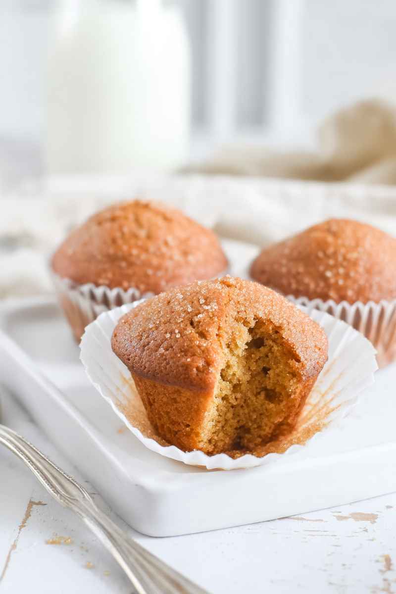 Golden-brown brown sugar muffins on a white plate, one cut open to reveal a soft, moist interior.