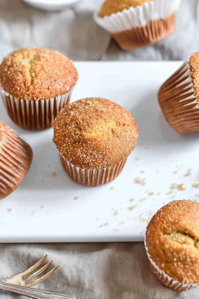 Golden-brown brown sugar muffins dusted with sugar, arranged on a white plate.