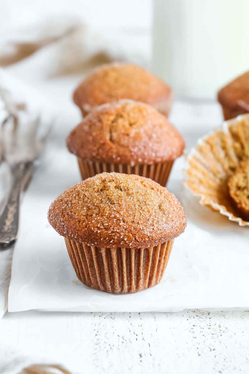 Baked brown sugar muffins with a golden crust, sitting on a white surface.