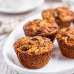 A plate of golden butter tart muffins, showcasing their moist texture and raisin-filled topping, served alongside a cup of coffee.