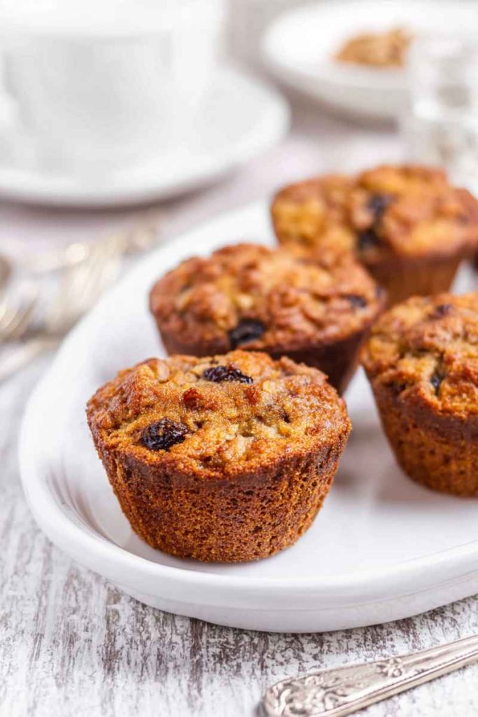 A plate of golden butter tart muffins, showcasing their moist texture and raisin-filled topping, served alongside a cup of coffee.