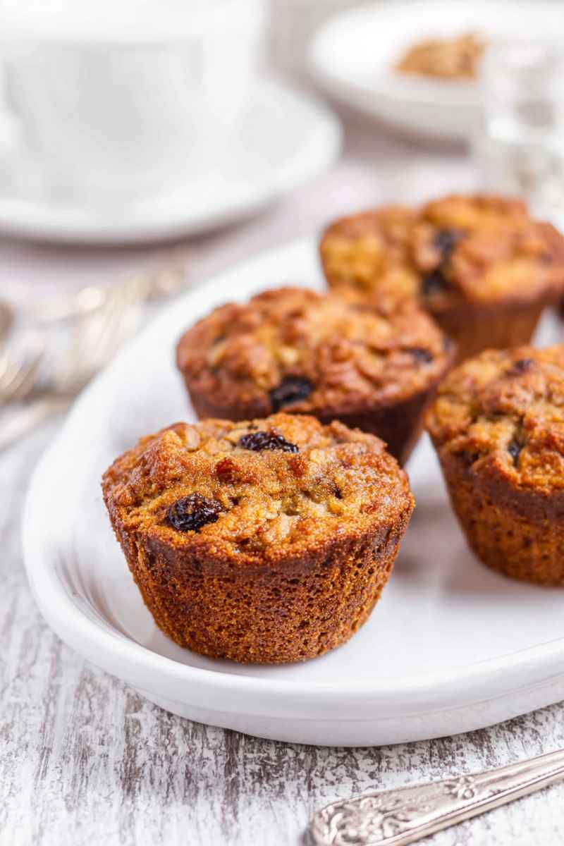 A plate of golden butter tart muffins, showcasing their moist texture and raisin-filled topping, served alongside a cup of coffee.