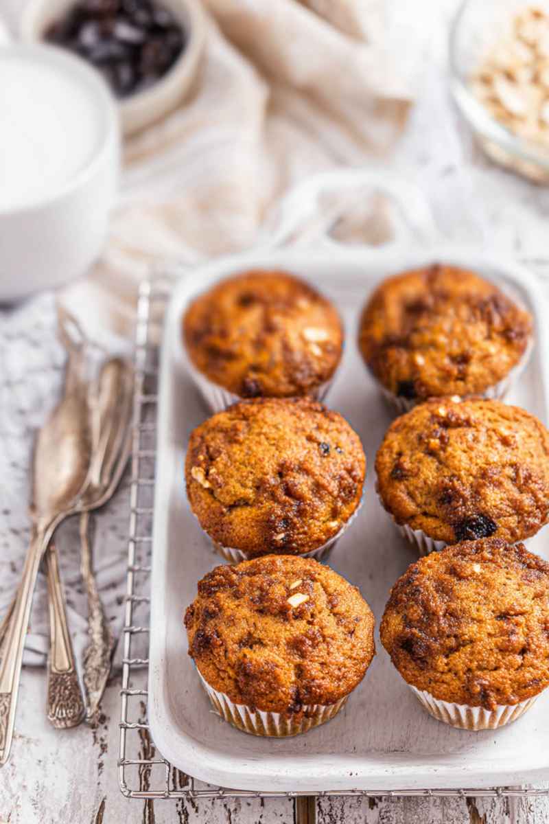 Six golden-brown butter tart muffins in white paper liners, arranged neatly on a white tray, ready to be enjoyed.