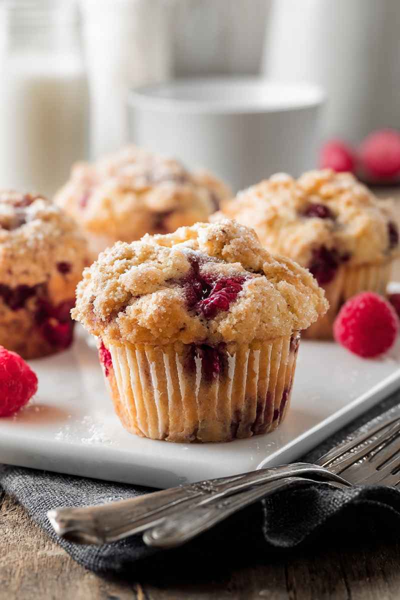 Fluffy buttermilk muffins filled with vibrant raspberries, dusted with powdered sugar, and served on a white tray.