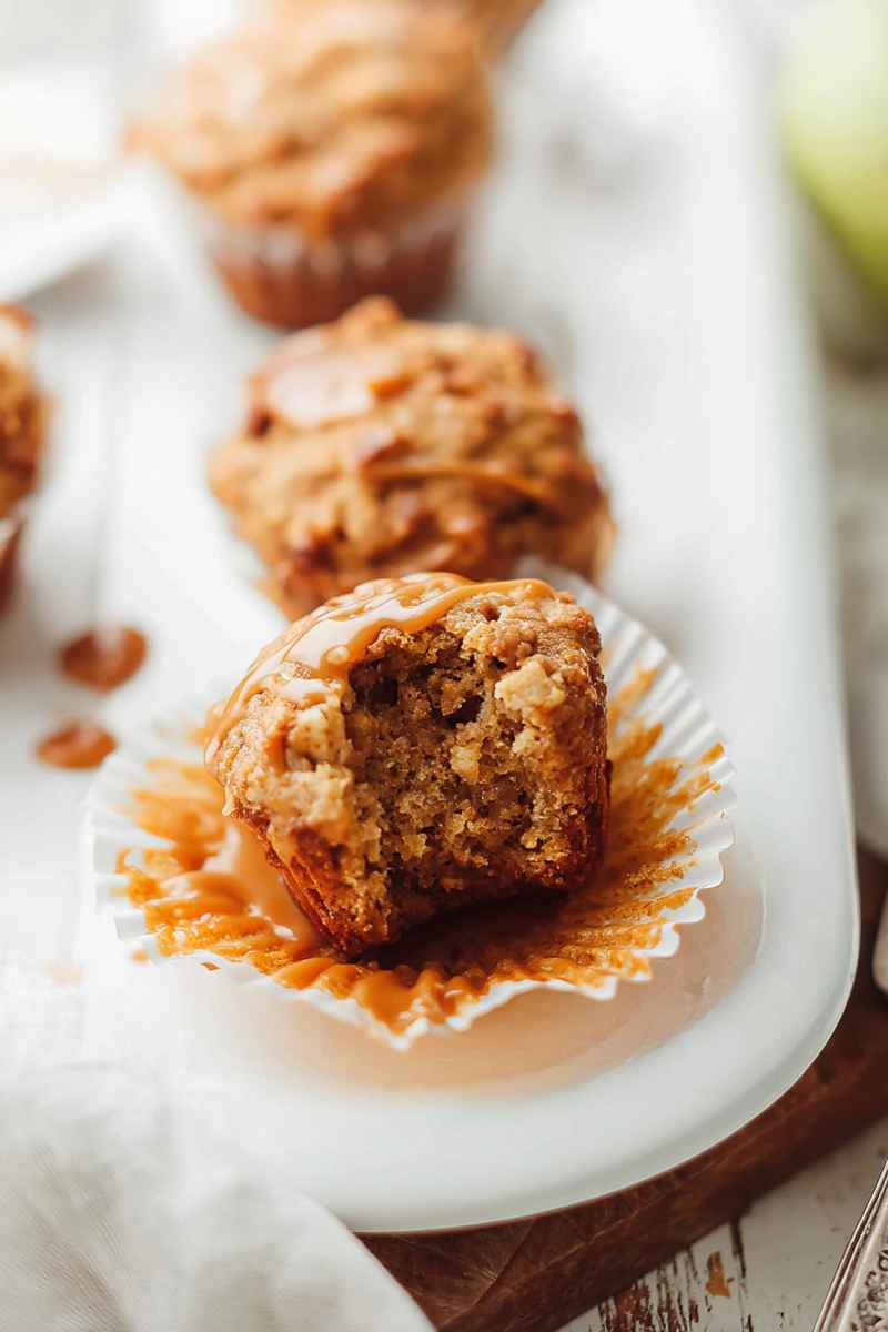 A partially eaten caramel apple muffin revealing its moist interior, topped with caramel sauce.