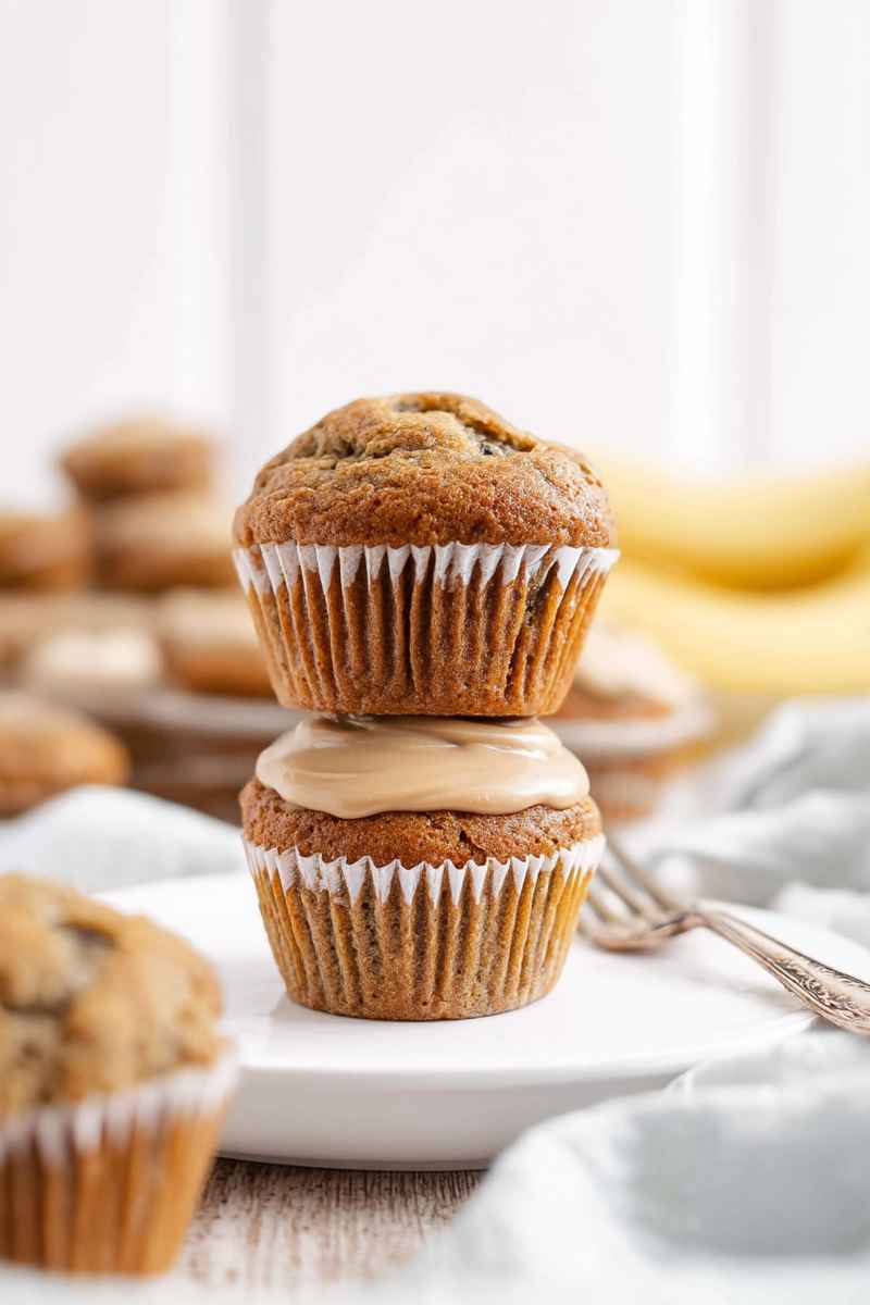Two caramel banana muffins stacked on a white plate, showcasing their golden-brown texture and caramel drizzle.