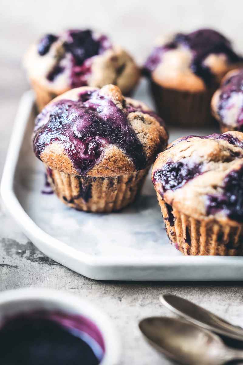 Cardamom-Spiced Blueberry Jam Muffins arranged on a white tray, topped with a purple glaze.