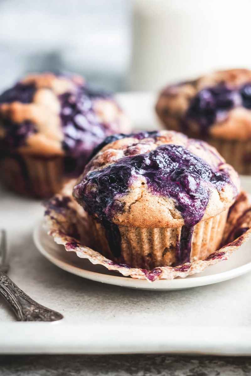 Close-up of a Cardamom-Spiced Blueberry Jam Muffin on a white plate, highlighting its fluffy texture and vibrant blueberry filling.