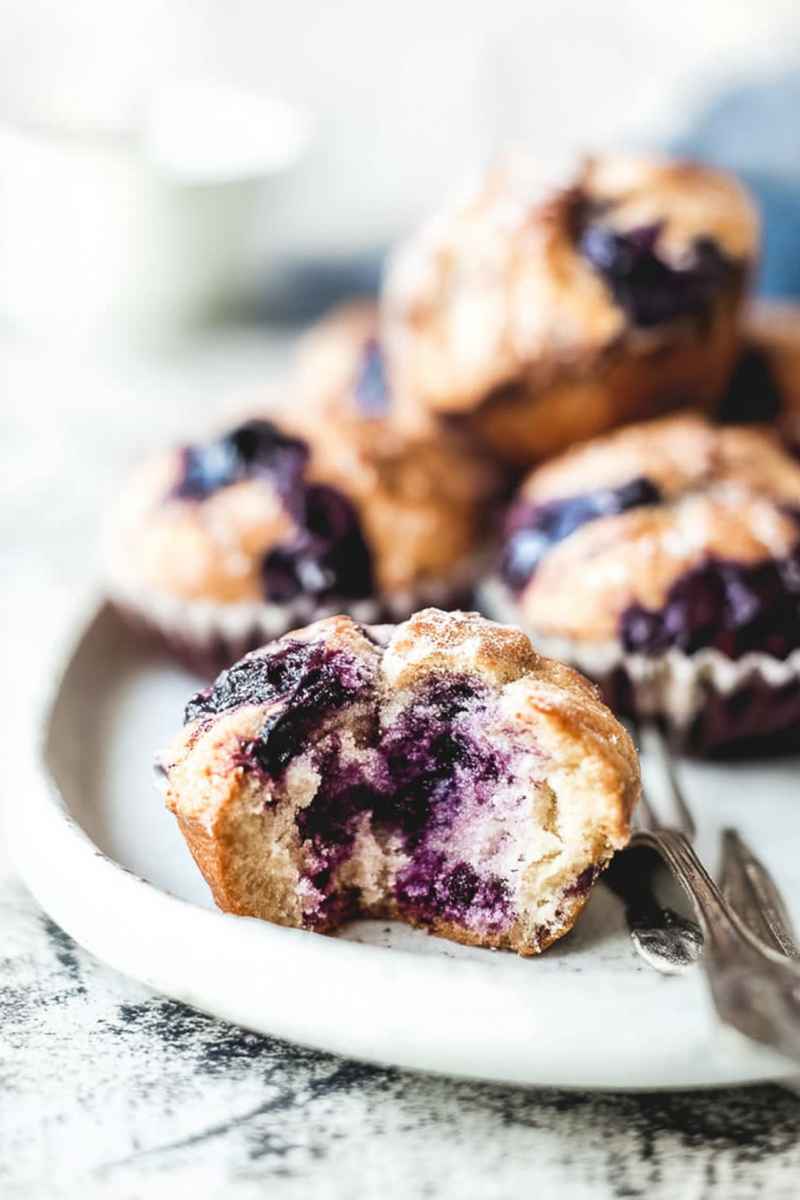Fluffy Cardamom-Spiced Blueberry Jam Muffins with a purple glaze, stacked on a white plate.