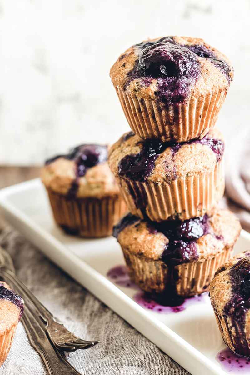 Three Cardamom-Spiced Blueberry Jam Muffins stacked on a white rectangular plate.