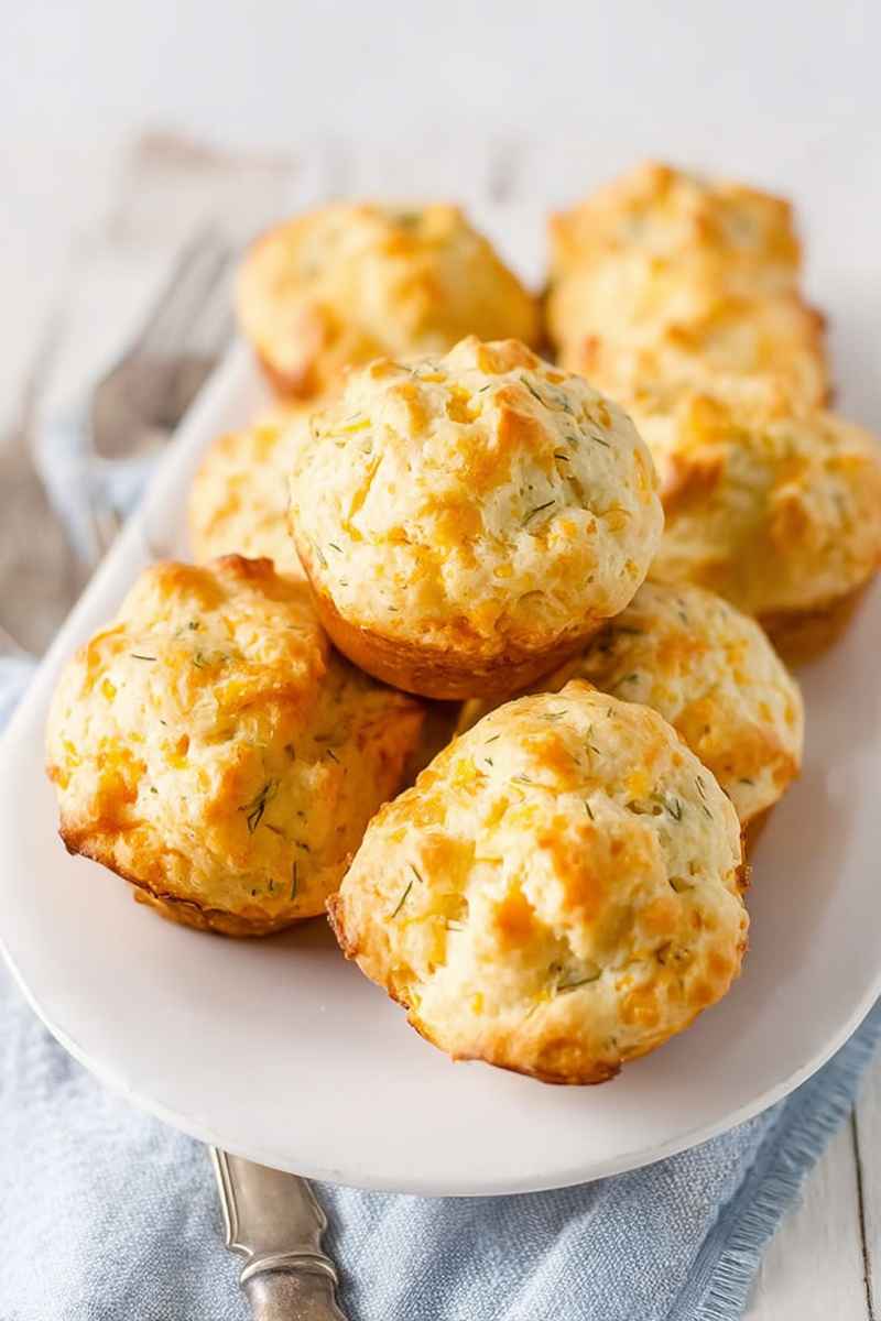 A plate piled high with golden Cheddar Dill Muffins, showcasing their fluffy texture and herb-topped appeal.
