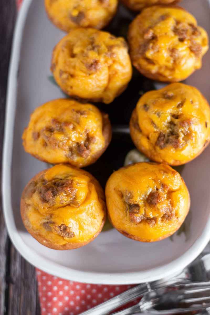A plate of golden-brown cheeseburger muffins topped with melted cheddar cheese and ground beef, ready to serve.