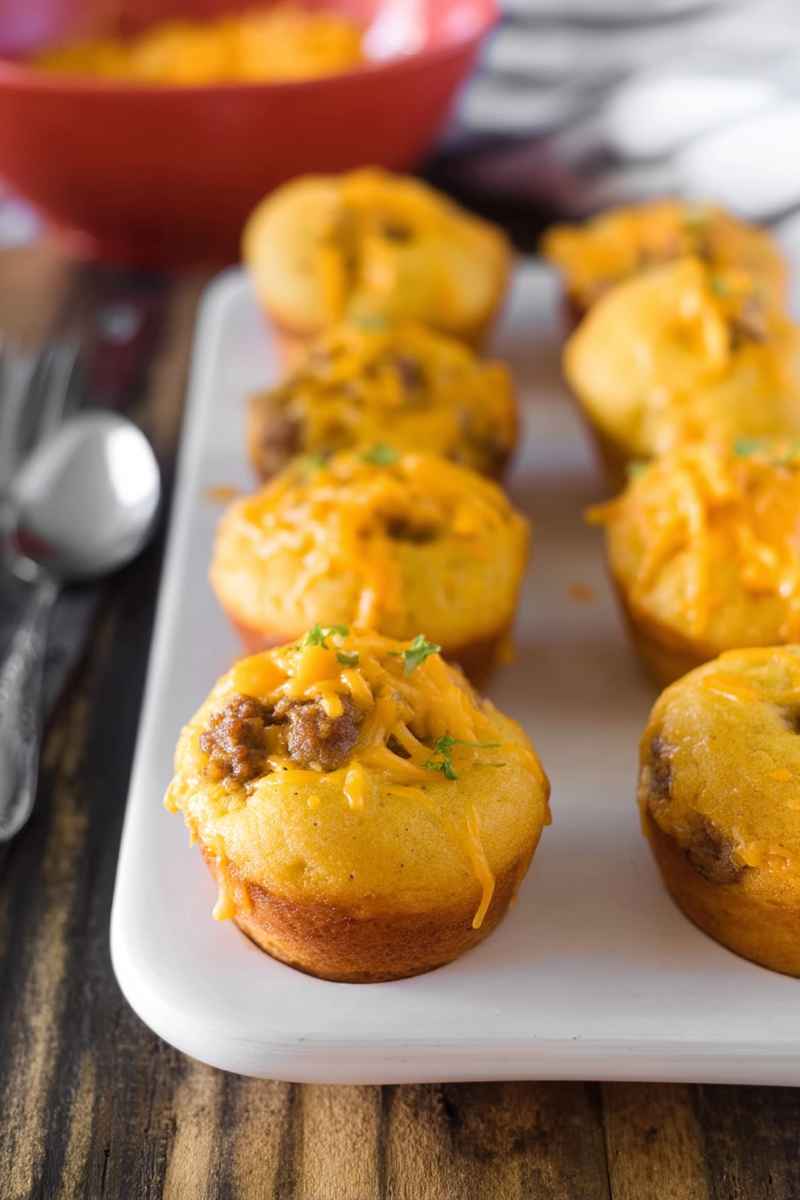 Cheeseburger muffins arranged neatly on a white platter, showcasing their golden crust and melted cheese topping.