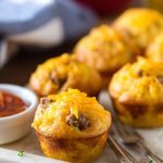 Cheeseburger muffins garnished with fresh herbs, served alongside a small bowl of ketchup.