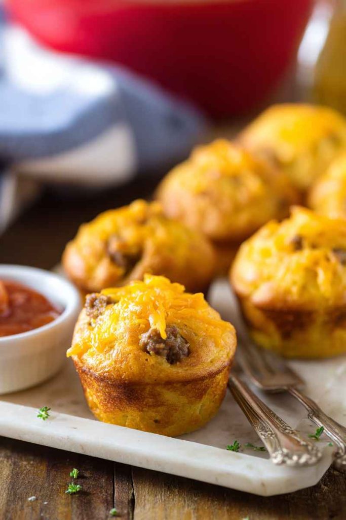 Cheeseburger muffins garnished with fresh herbs, served alongside a small bowl of ketchup.