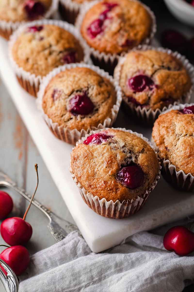 A tray of freshly baked cherry muffins with bright red cherries scattered around, highlighting their natural charm.