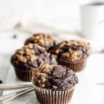 Dark, moist muffins topped with a crunchy toffee streusel, set against a clean, bright background.