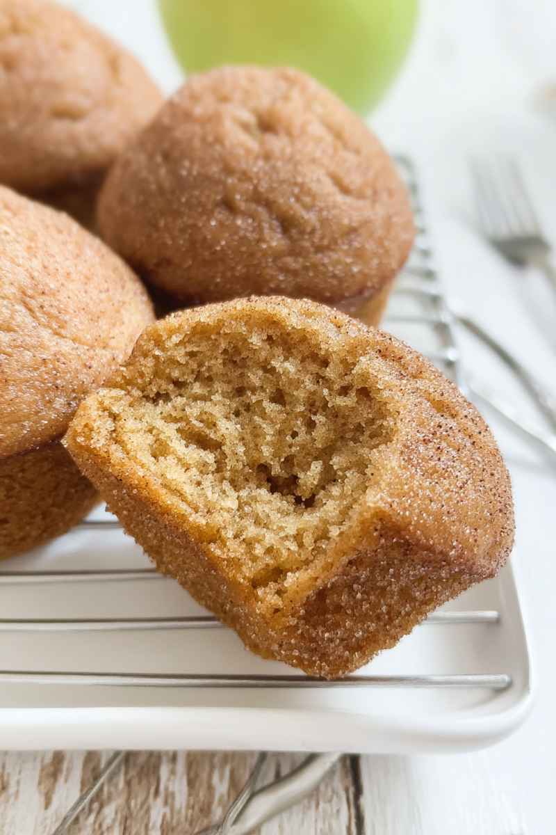 A close-up of a halved cinnamon applesauce muffin revealing its light, airy interior and golden-brown exterior coated in cinnamon sugar.