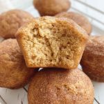 A stack of cinnamon applesauce muffins on a cooling rack, each generously coated in cinnamon sugar, with one muffin cut open to show its fluffy interior.