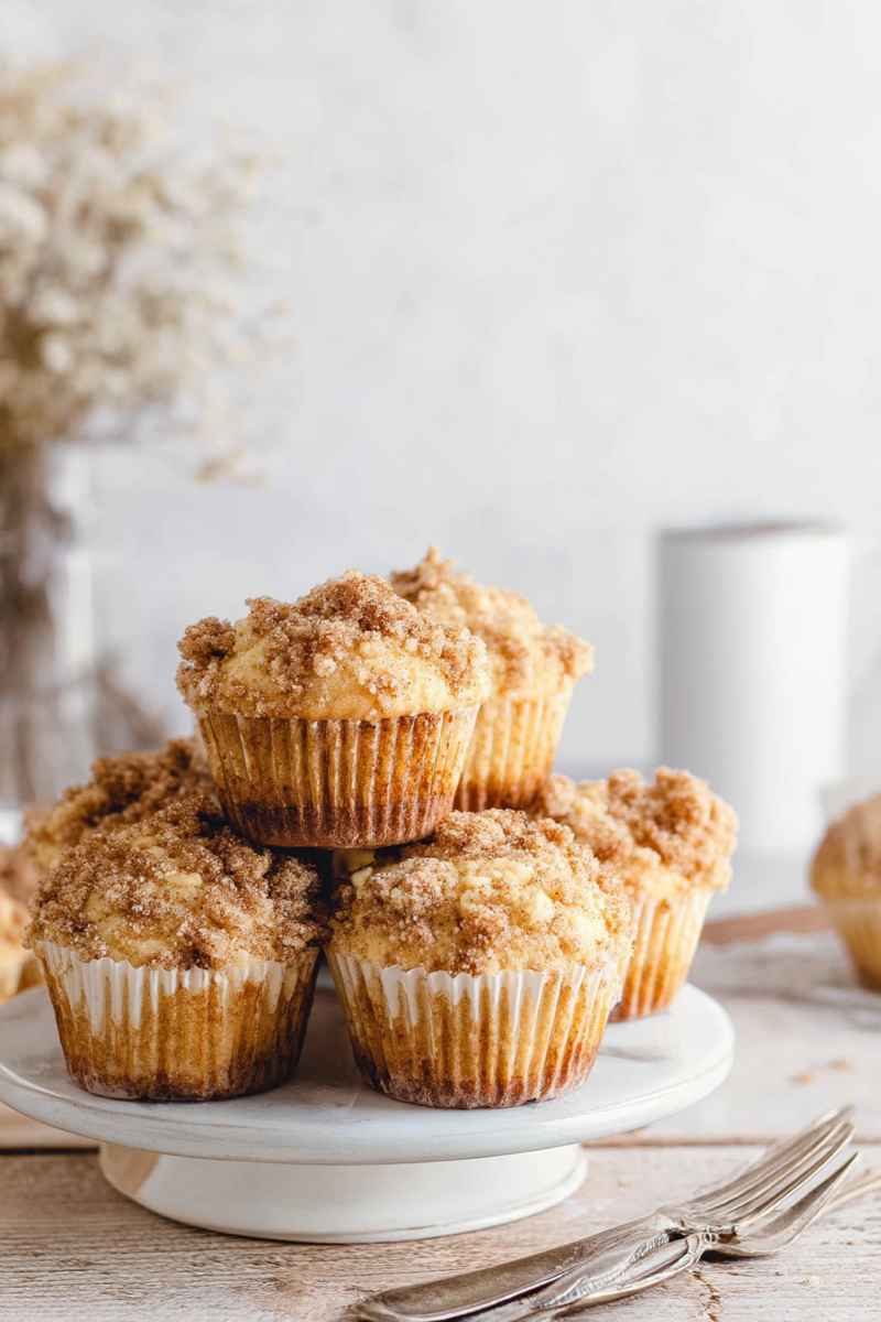 Stacked cinnamon streusel muffins on a white cake stand, ready to be enjoyed.